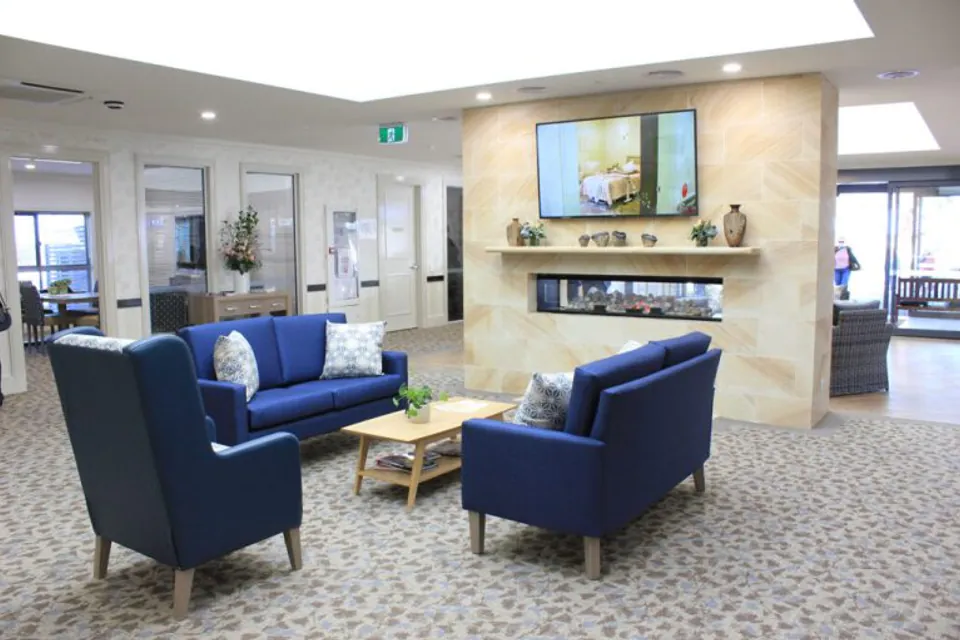 Communal lounge with blue sofas and armchairs around a fireplace.