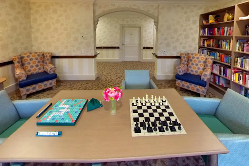 Games table with a chessboard beside lounge chairs and bookshelves.