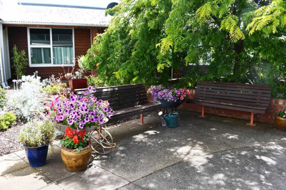 Garden benches surrounded by flowers and leafy trees.