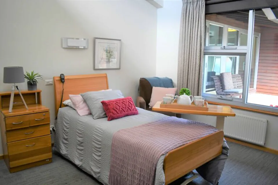 Resident bedroom with a bed, bedside cabinet and window view.