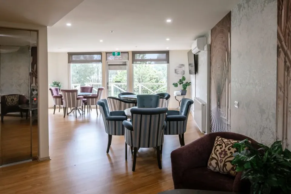 Communal sitting and dining area beside garden windows.