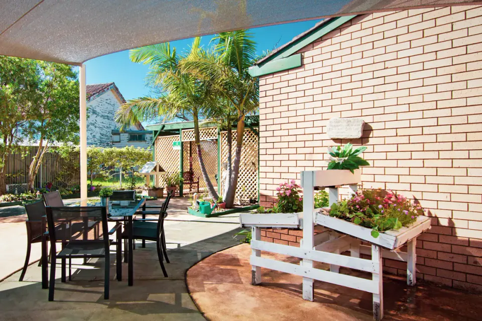 Shaded outdoor terrace with a table and chairs under a shade sail, a raised garden planter and palm trees