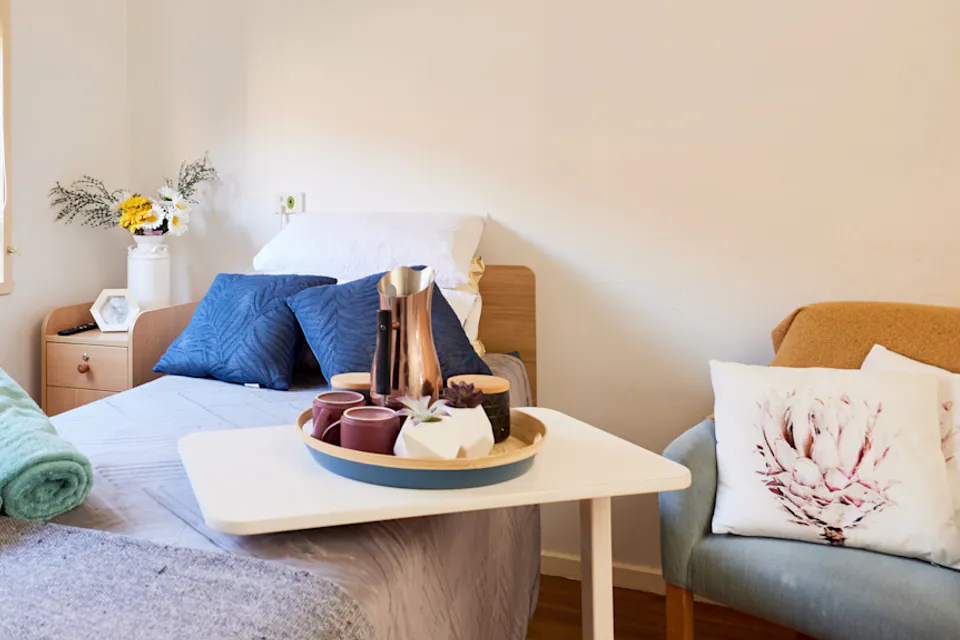 Care bedroom with a made bed and armchair