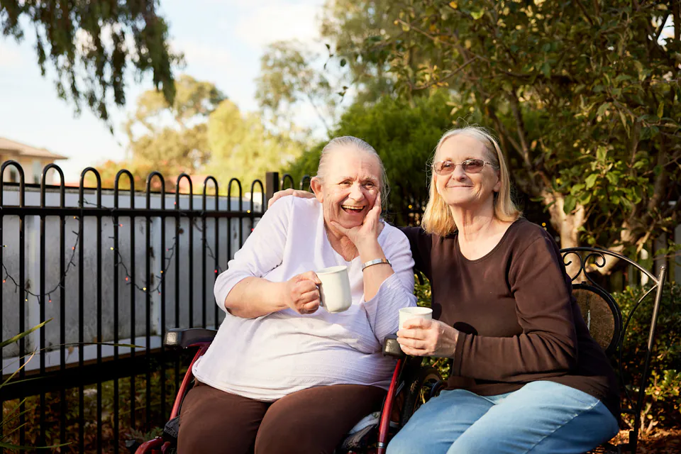 Two older women talking over drinks in a garden