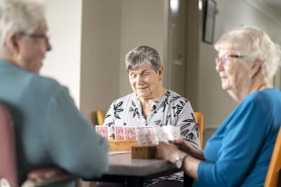 Three older women playing cards around a table