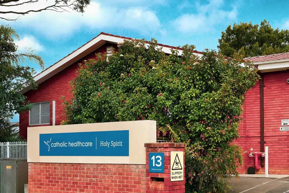 Red brick building with a tiled roof and a signboard at the street entrance, beside a white gate