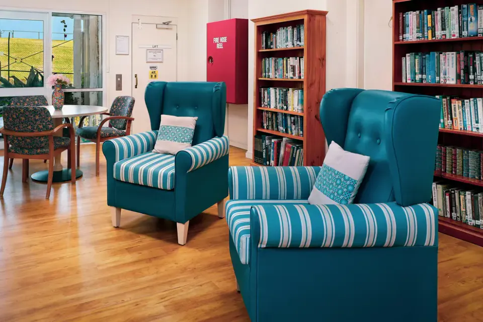 Sitting area with teal armchairs, bookshelves, a television and glass doors to a grassed area