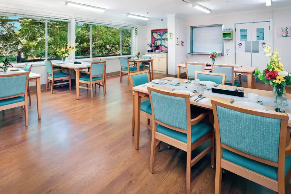 Dining room with timber tables set for a meal, teal chairs and wide windows looking onto trees
