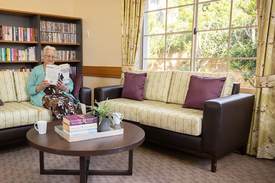 Person seated in a lounge beside a bookshelf