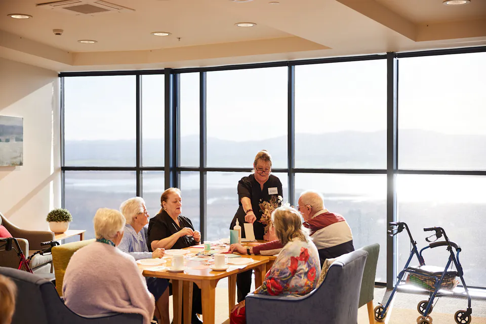 Residents and care worker sharing a table by large windows
