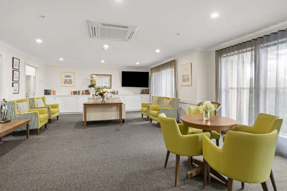 Communal lounge with green chairs, sofas and television.
