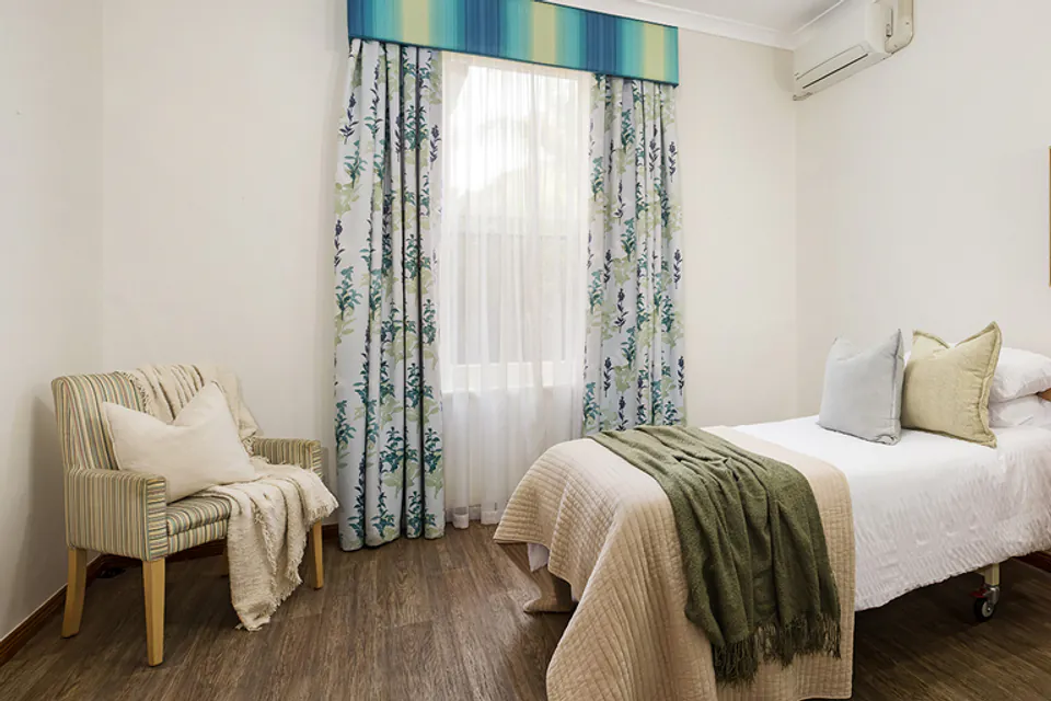 Bedroom with a single bed, armchair and curtained window