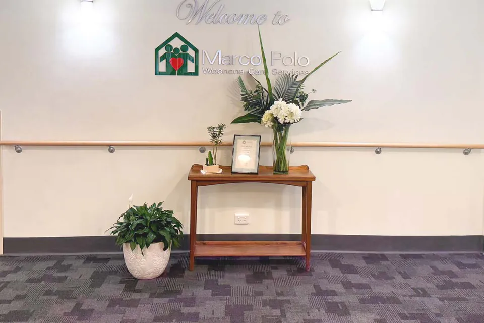 Foyer wall with a welcome sign above a table of flowers and plants