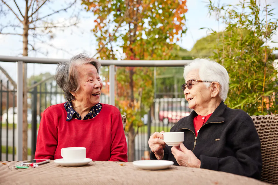 Two older women talking over tea at an outdoor table