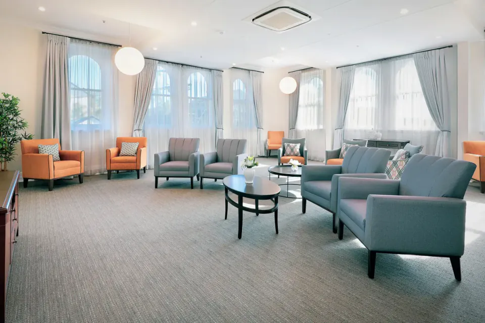 Lounge with grey and orange armchairs around low tables beside tall curtained windows