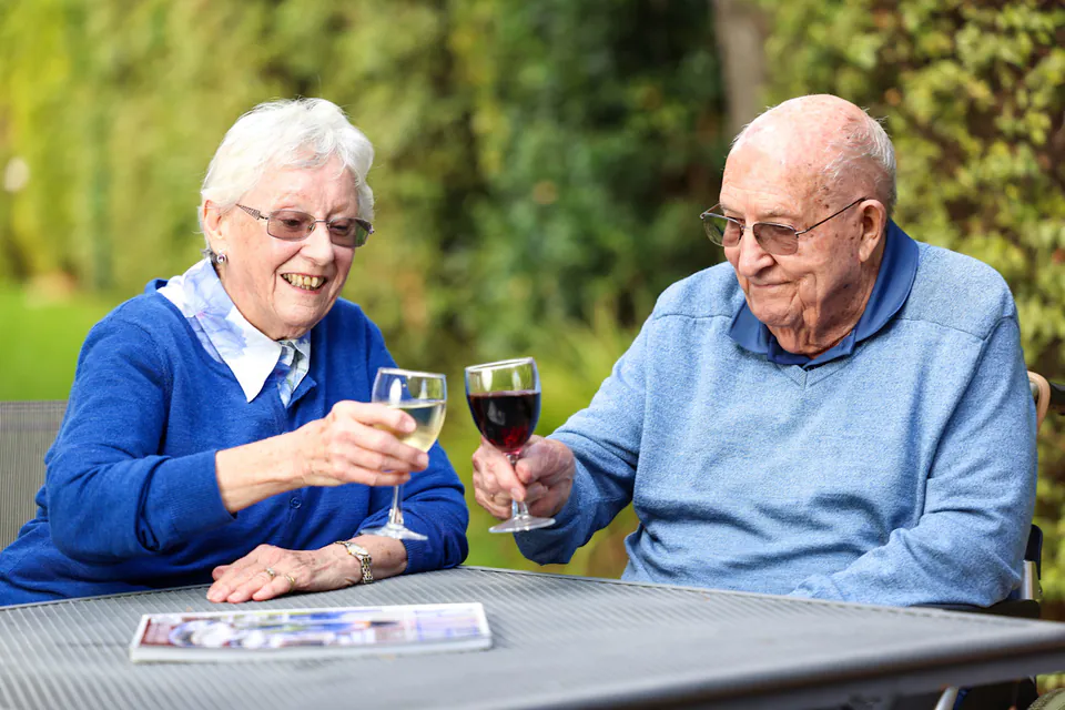 Two older adults sharing a drink at an outdoor table