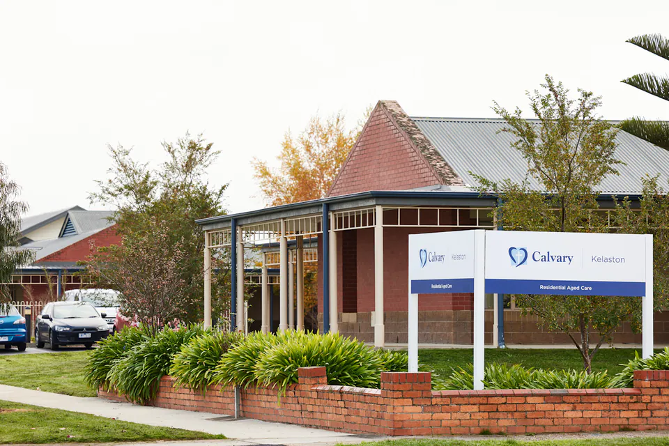 Brick building entrance behind a roadside sign and garden